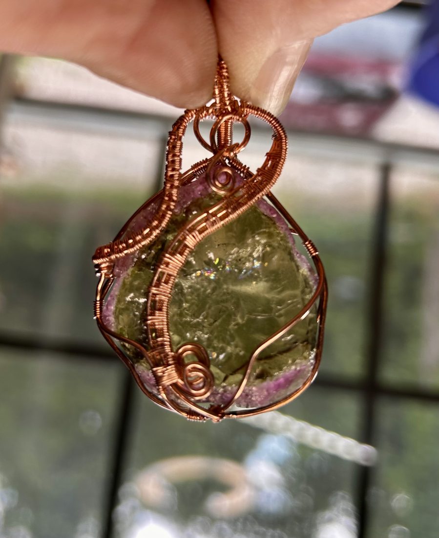 Wire-wrapped green stone pendant held in hand